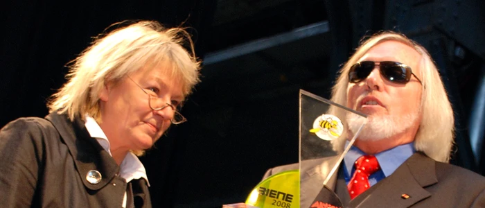 Blinder-weißhaariger Werner Hirschmann übergibt transparent-gelben Preis an Gaby Schäfer.