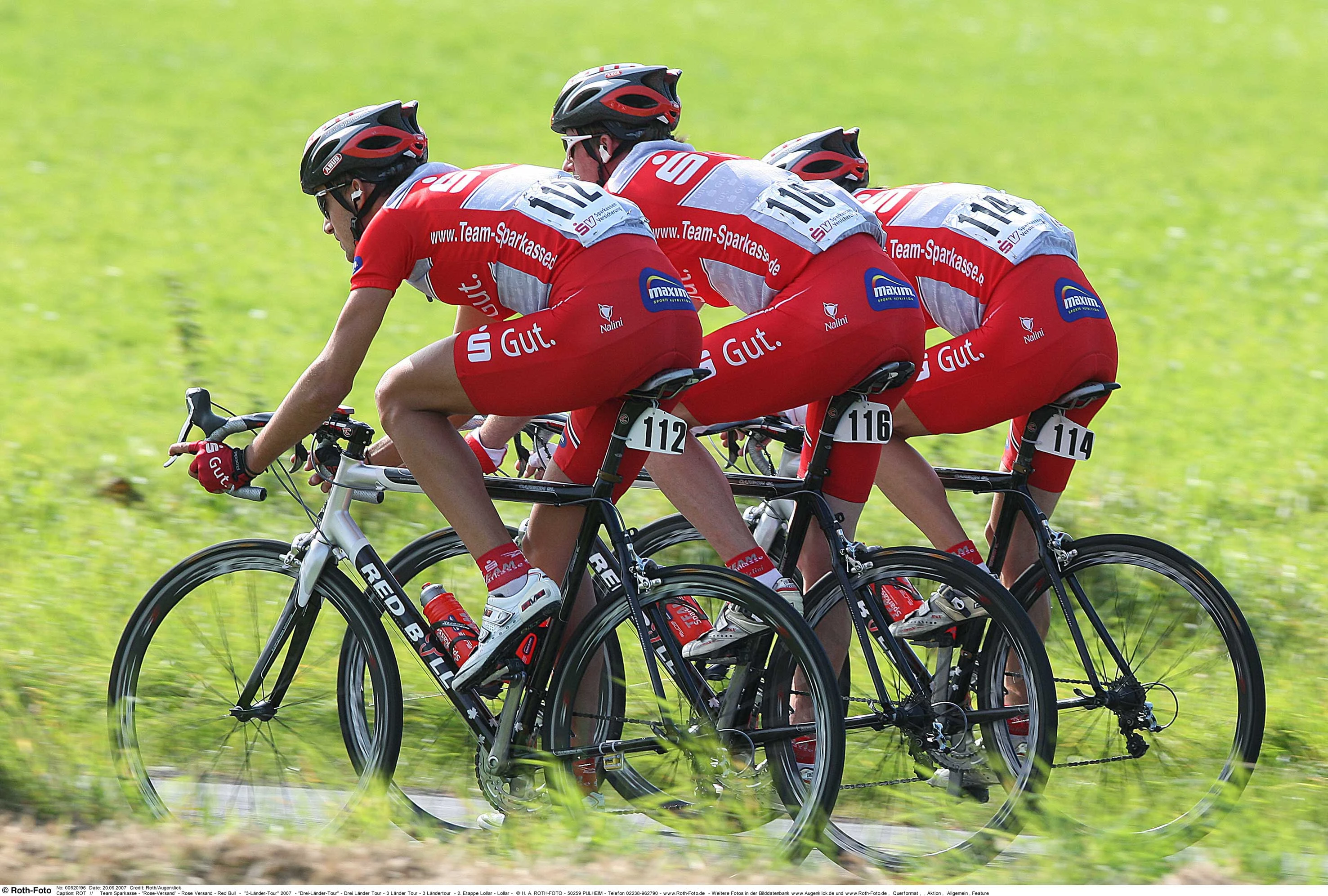 Drei Radrennsportler des Teams Sparkasse im roten Dress auf schwarzen Rädern.