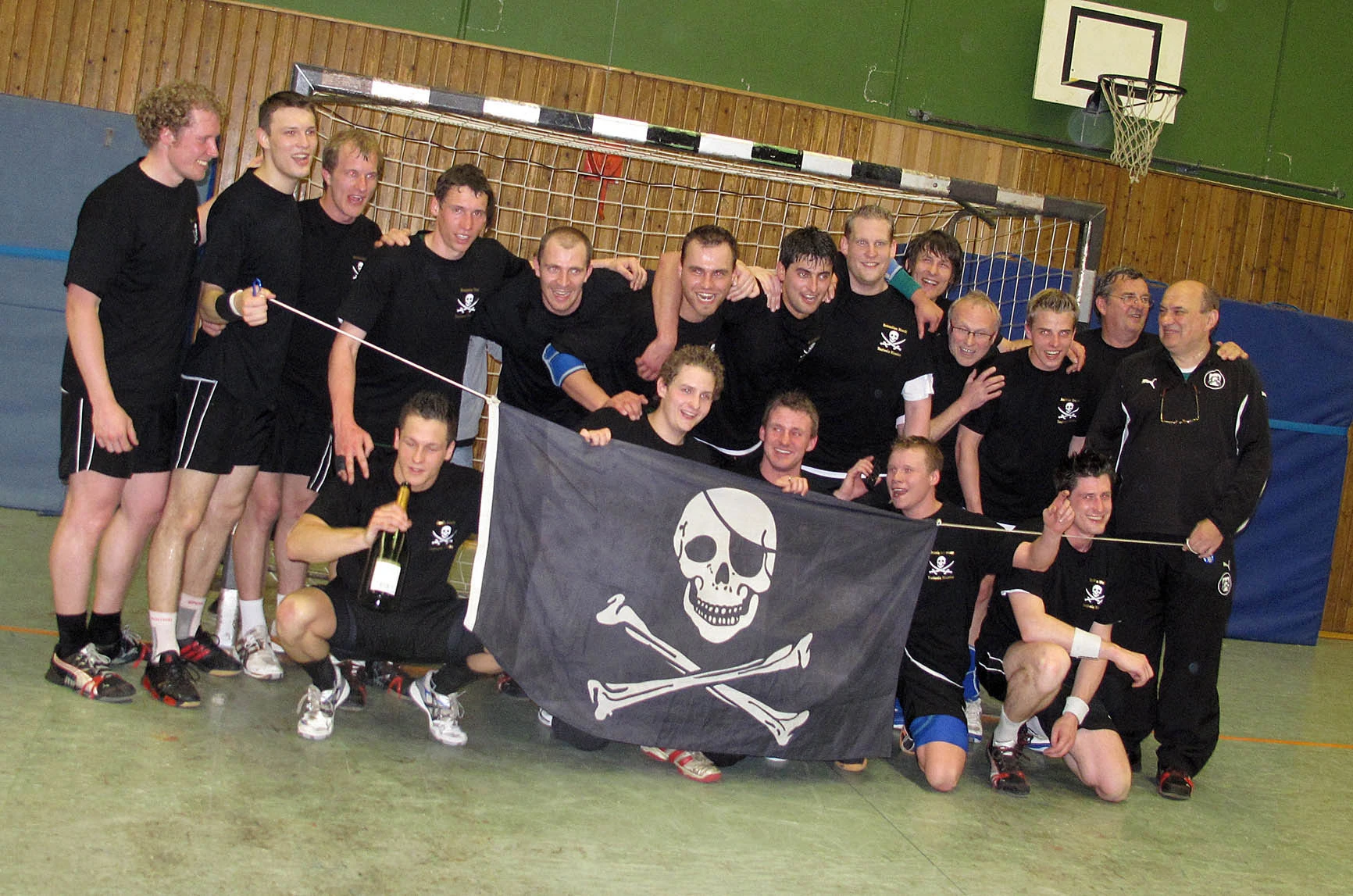 Jubelnde Handballer mit schwarzen Shirts im Handballtor halten eine Piratenflagge hoch.