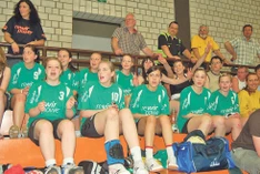 Applaudierende Handballerinnen in grünen Trikots auf der Tribüne sitzend