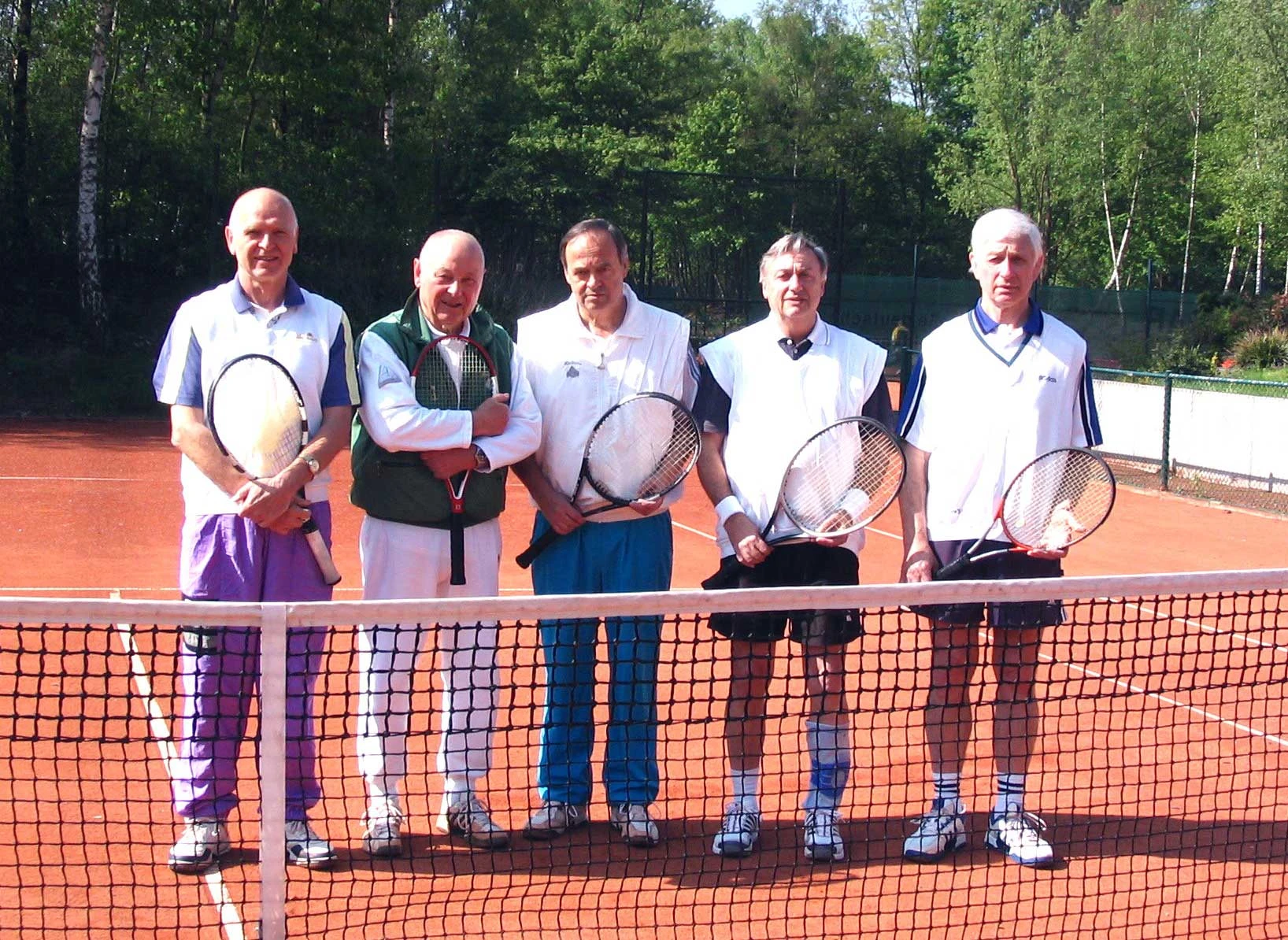 Fünf älere Tennisspieler mit ihrem Schläger auf roter Asche vor dem Netz