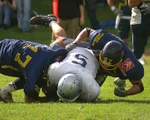 Drei American Footballer kämpfen auf der Wiese liegend um das Ei.