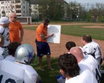 Trainer steht mit Headset und Schautafel vor seinen Spielern