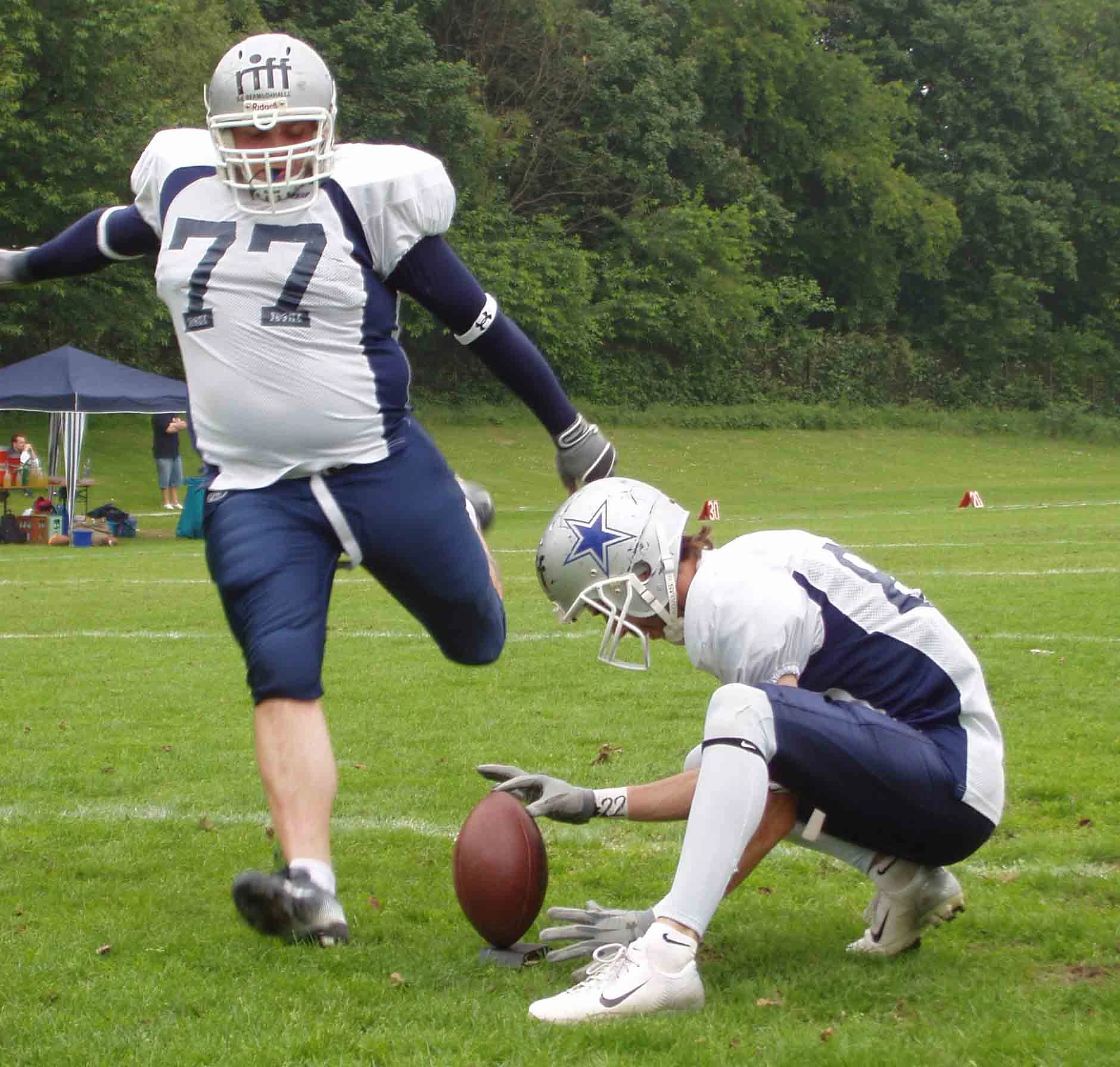 Kicker beim American Football tritt von seinem Teamkollegen gehaltenes Lederei.