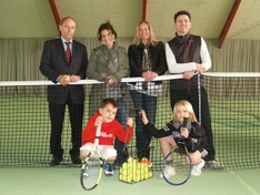 Vier Erwachsene hinter und zwei Kinder vor einem Tennisnetz