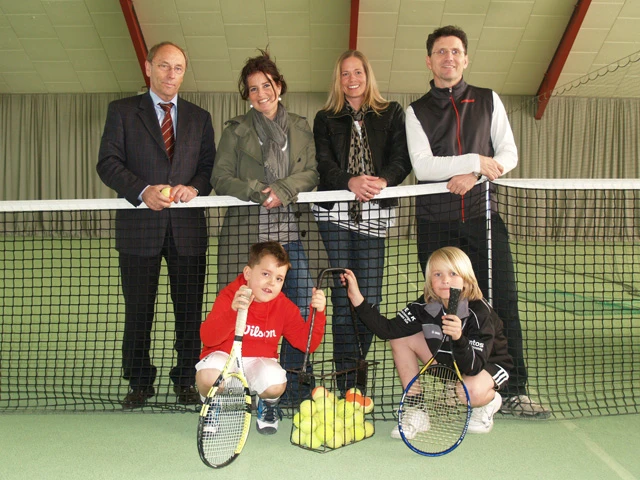 Vier Erwachsene hinter und zwei Kinder vor einem Tennisnetz