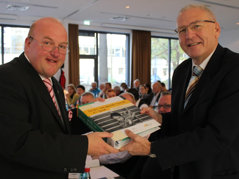 Der dsj-Vorsitzende Ingo Weiss (l.) übergibt den Ordner mit Materialien zur Prävention sexualisierter Gewalt an DOSB-Generaldirektor Michael Vesper.