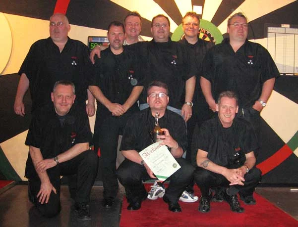 Neun Dartspieler, schwarz gekleidet, mit Urkunde und Pokal am Dartbrett.