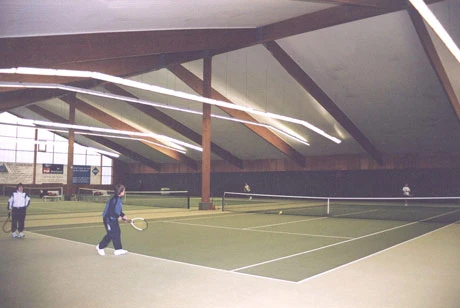 Tennishalle mit weißer Decke und grünem Filzboden.