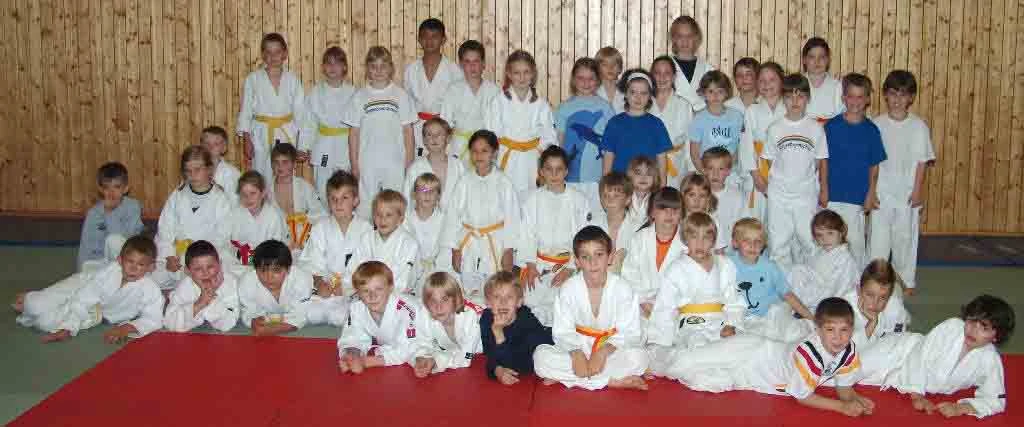 Gruppe junger Judoka in ihren weißen Kampfanzügen in einer Sporthalle.